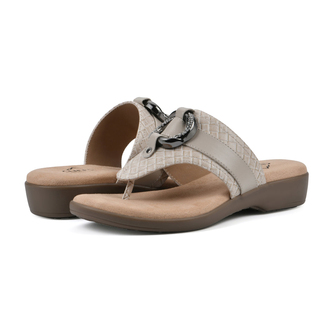Angle view of a pair of light beige thong sandals with a centered metal ring ornament and tan sole