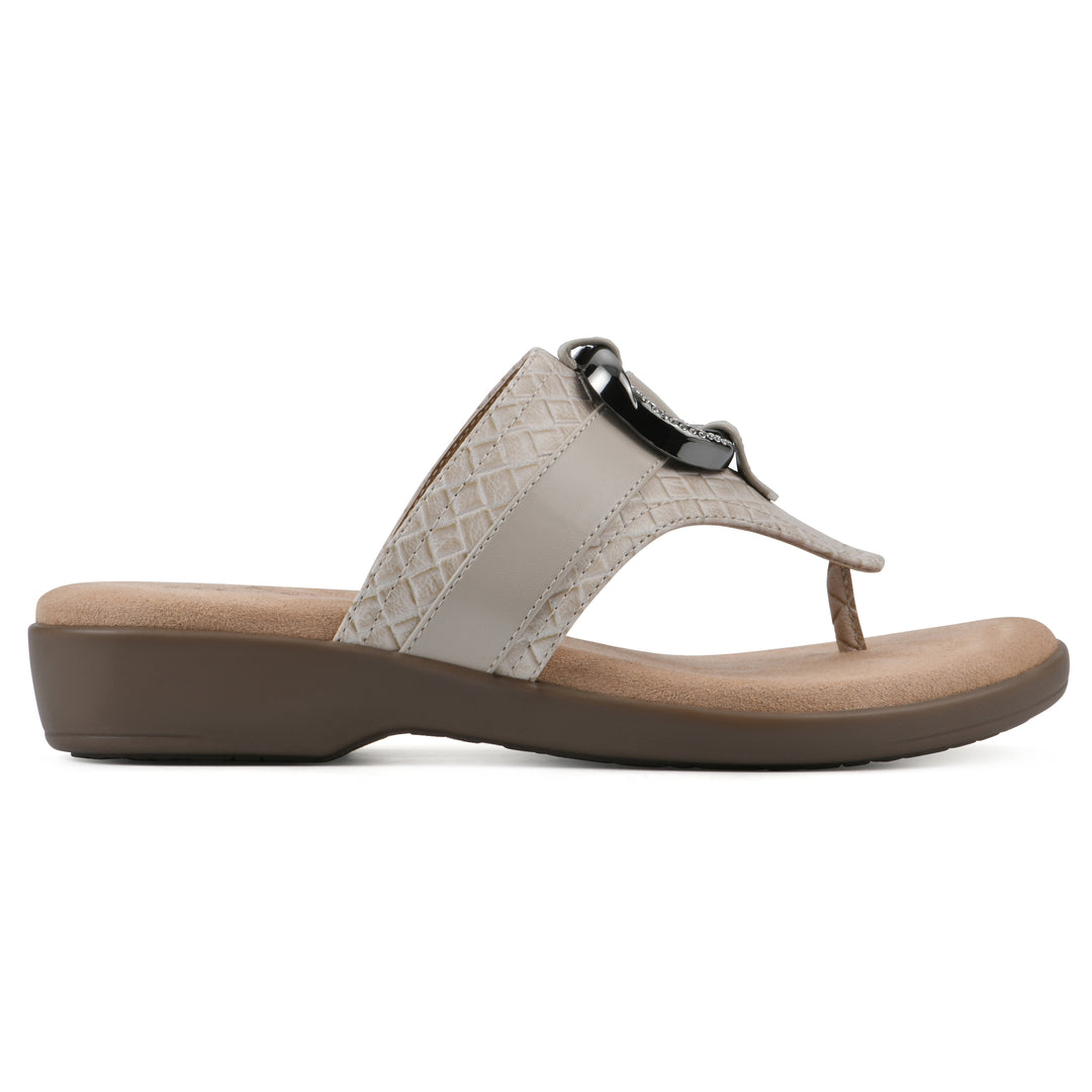 Side view of a light beige thong sandal with a centered metal ring ornament and tan sole