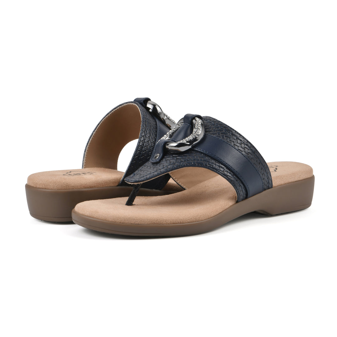 Angle view of a pair of navy thong sandals with a centered metal ring ornament and tan sole