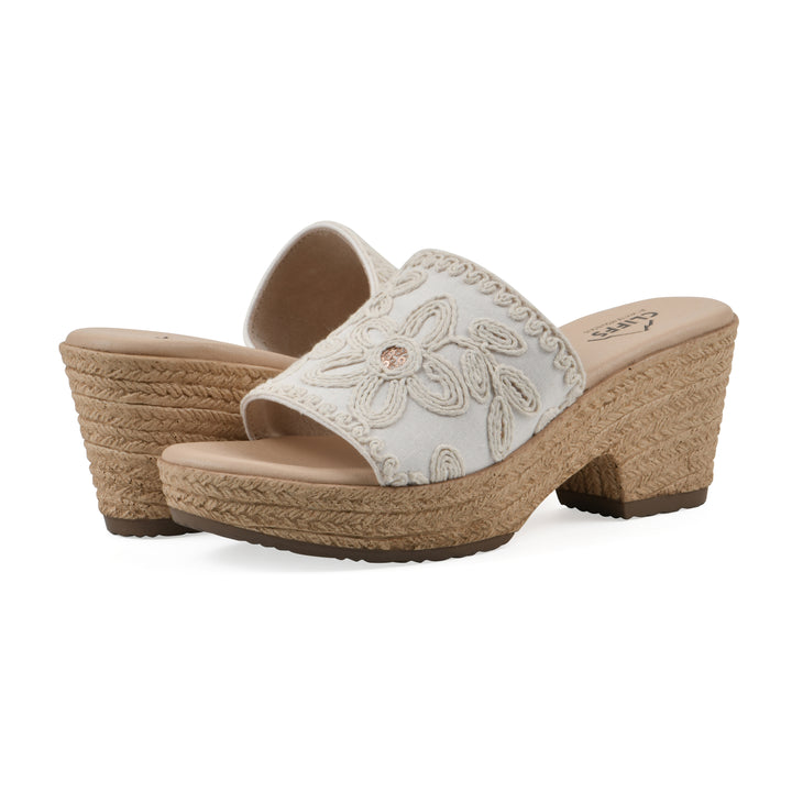 Angle view of a pair of white wedge sandals with cream embroidered floral pattern and a braided rope-style sole