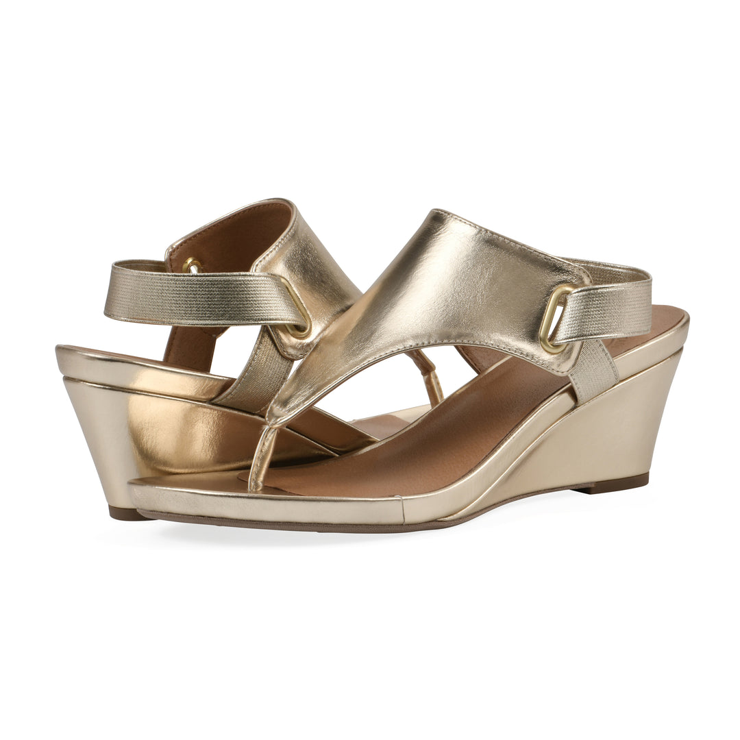 Angle view of a pair of gold metallic thong wedge sandals with a wrapped heel, elastic ankle strap, and gold sole