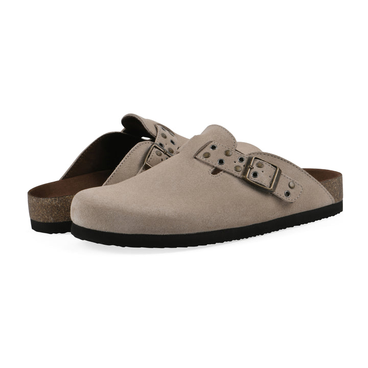 Angle view of a pair of tan suede backless clogs with an adjustable buckle strap with stud and eyelet detailing and a black sole
