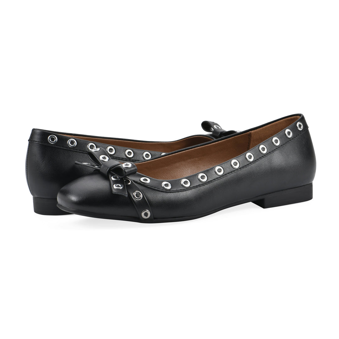 Angle view of pair of black faux leather flats with small, centered bow, silver metal grommet lining and a black sole