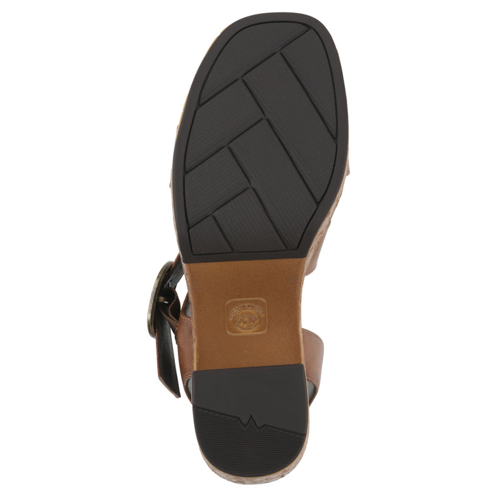 Sole view of a brown platform sandal with ankle buckle, a brown, faux cork sole, and black patterned sole bottom