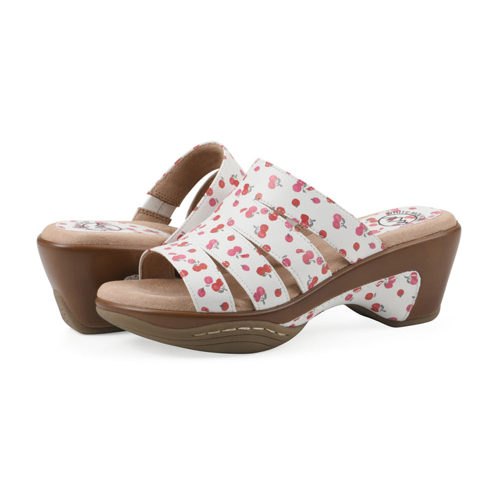 Angle view of a pair of open-toe mule sandal in white with a red cherry pattern, a cushioned insole, and a brown heel 
