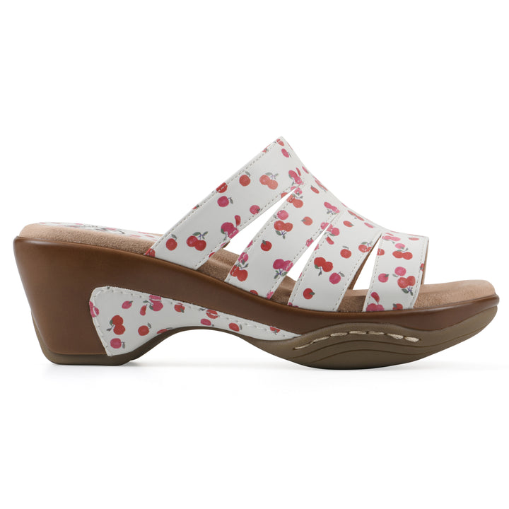 Side view of an open-toe mule sandal in white with a red cherry pattern, a cushioned insole, and a brown heel 